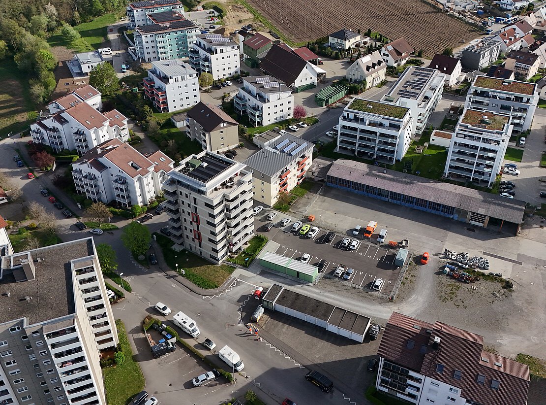 Modernes Wohngebiet mit Solaranlagen und Parkfläche Luftaufnahme eines Wohngebiets mit mehrgeschossigen Wohnhäusern, begrünten Dächern, Solaranlagen und einem Parkplatz mit mehreren Fahrzeugen.